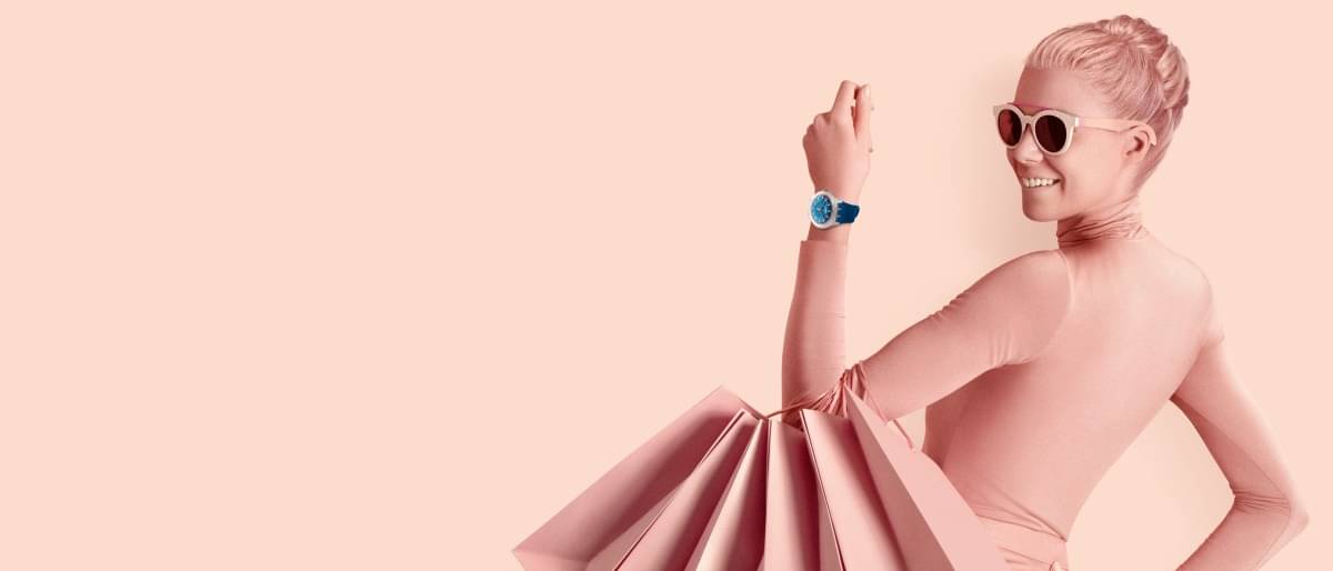Frau in rosa Kleidung mit Einkaustaschen am Arm hält ihre Smartwatch in die Höhe
