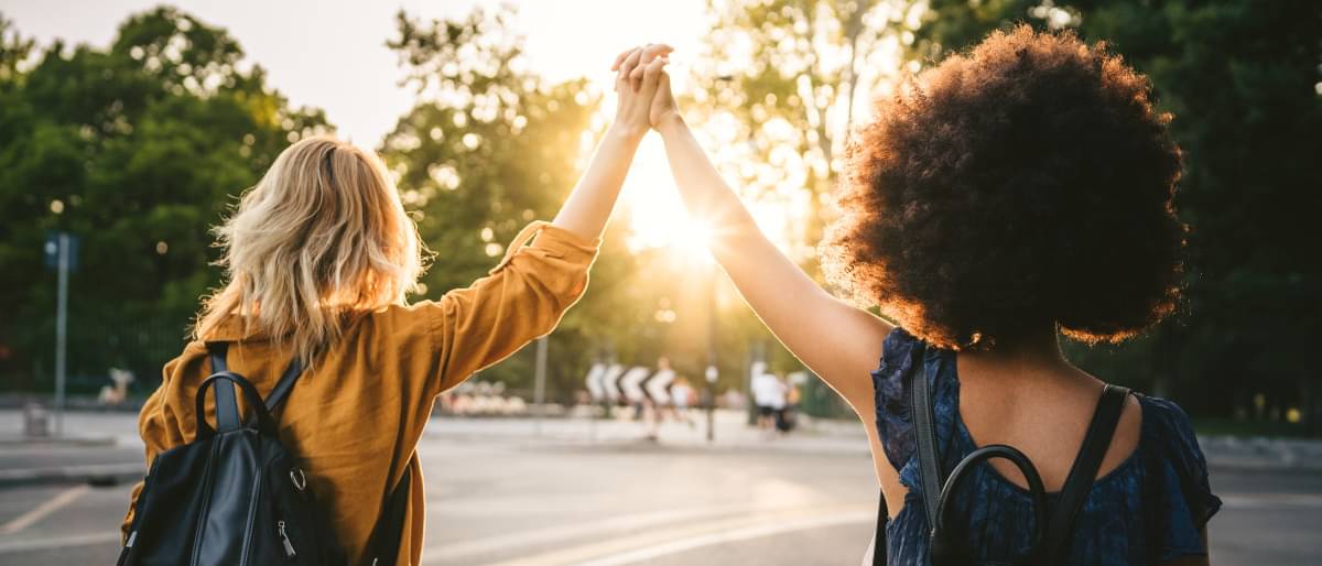 Zwei junge Frauen laufen an einer Straße entlang und halten gemeinsam ihre Händein die Luft 