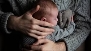 Ein Vater hält sein schlafendes Baby liebevoll vor dem Bauch.