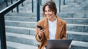 Junge Frau sitzt auf einer Treppe und checkt ihre ETFs auf ihrem Smartphone ab.