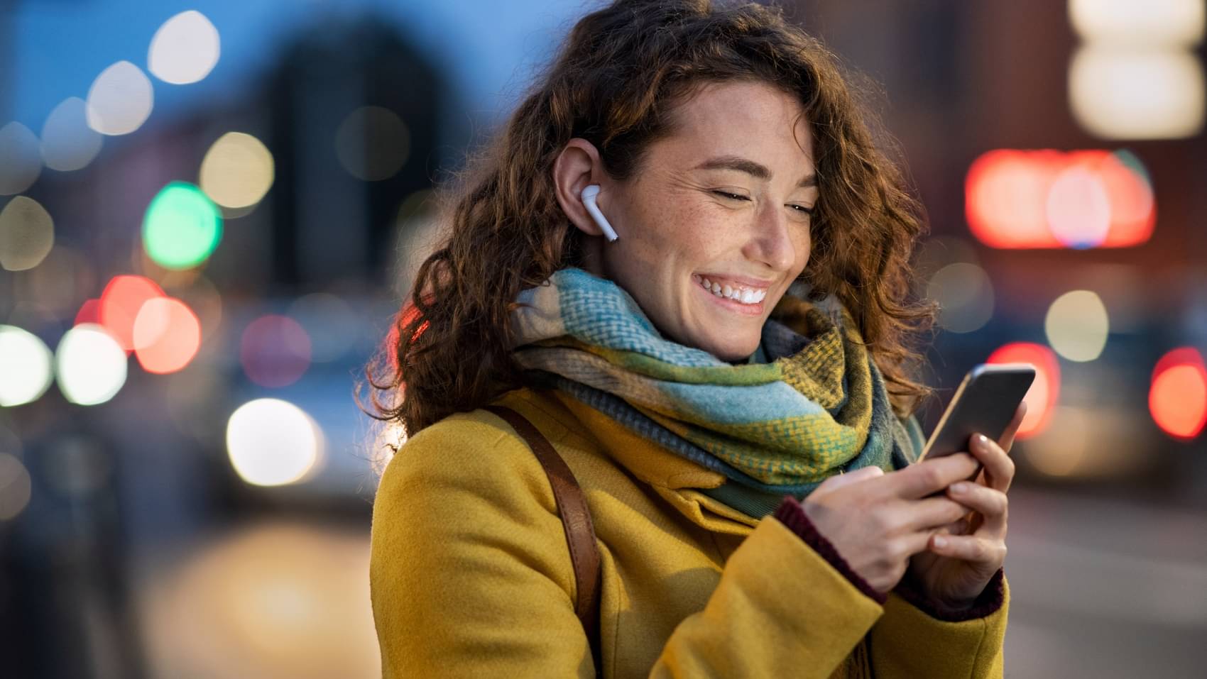 Junge Frau mit Kopfhörern schaut auf ihr Handy