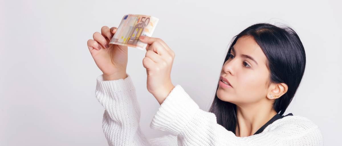 Eine Frau schaut sich einen Geldschein an - Falschgeld erkennen