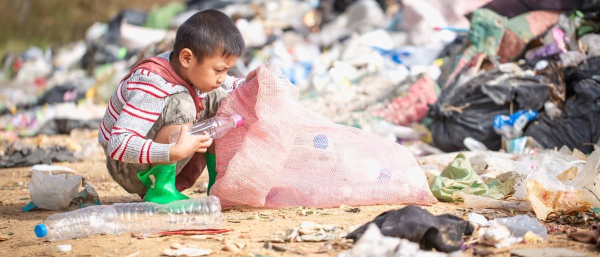 Ein kleiner Junge sammelt Plastikflaschen auf einem Müllplatz