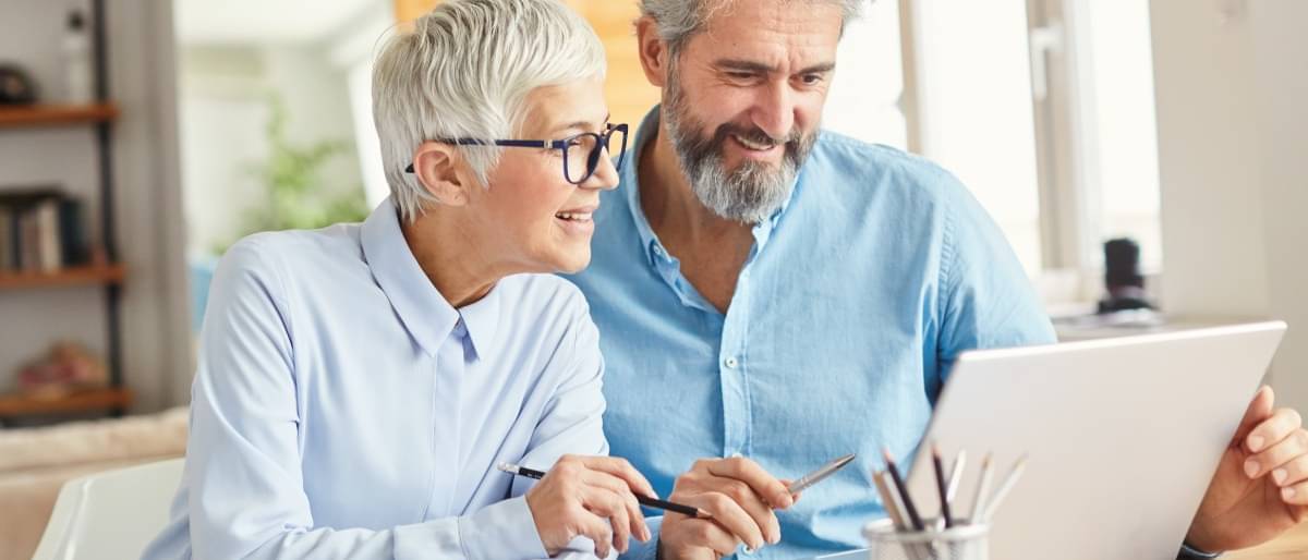 Ein älteres Paar sitzt vor einem Laptop und berechnet seine Rentenpunkte