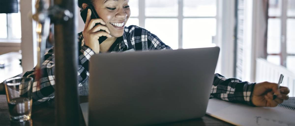 Eine junge Unternehmerin sitzt lächelnd vor dem Laptop und telefoniert