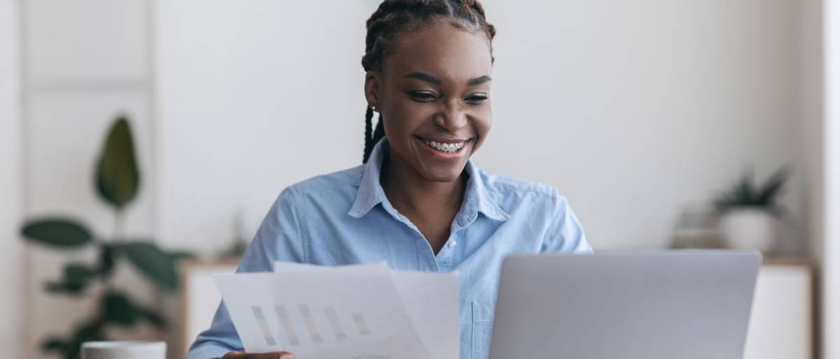 Junge Frau mit Zahnspange schaut lächelnd auf ihren Laptop und informiert sich über Aktien