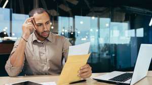 Ein Mann sitzt im Büro an seinem Schreibtisch und liest aufmerksam und mit einem nachdenklichen Blick einen Brief.
