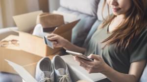 Eine junge Frau hat einige Kleidungsstücke eingekauft und rechnet nun ihre Ausgaben zusammen.