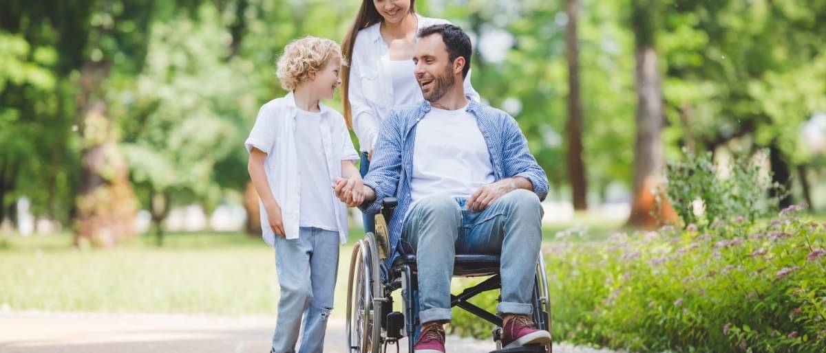 Eine Familie geht im Park spazieren, der Vater wird im Rollstuhl geschoben.