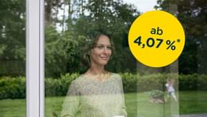 Frau steht mit ihrer Kaffeetasse am Fenster schaut ihrer Tochter beim Spielen zu: Baufinanzierung ab 4,07 % p.a.*