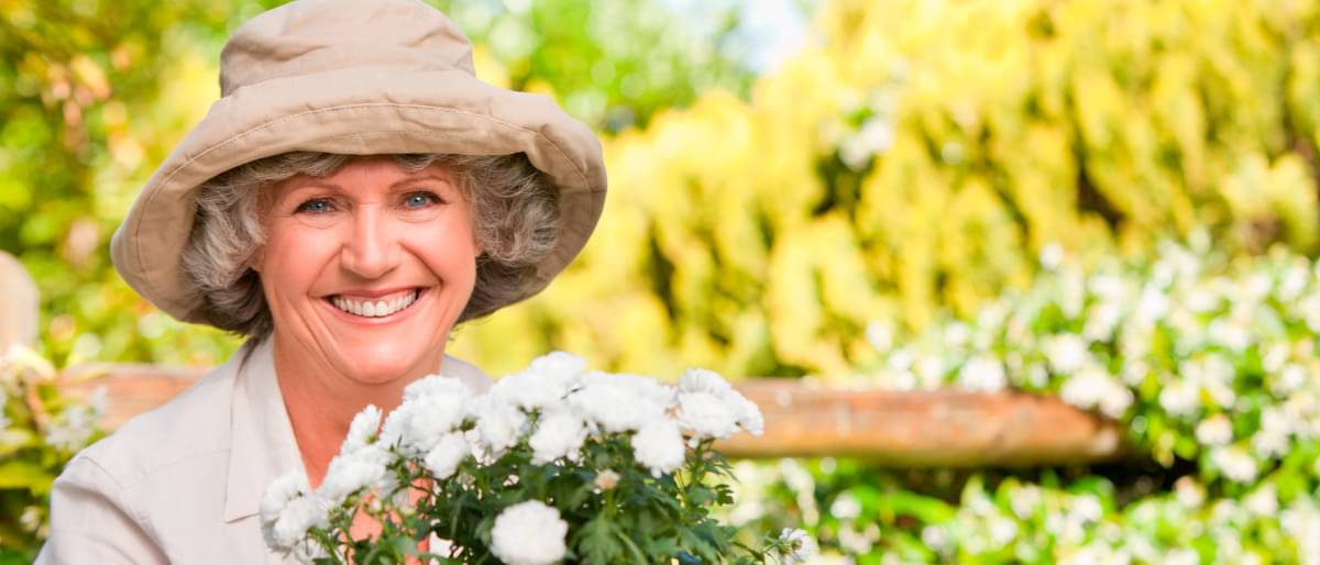 Eine Frau mit Hut und einem Blumenstrauß lächelt in die Kamera - Kosten Zahnprothese 