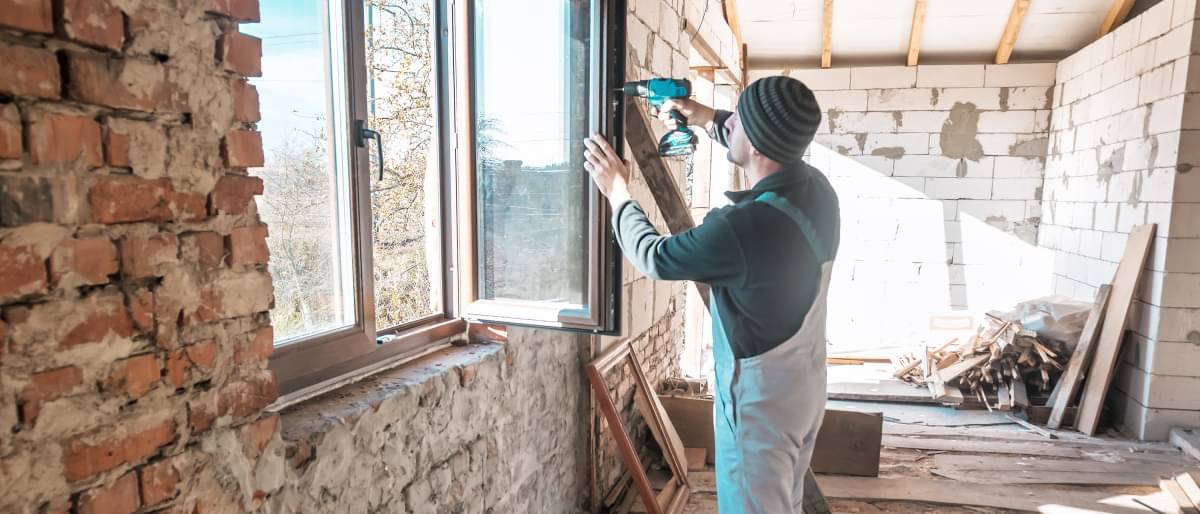 Ein Arbeiter schraubt an einem Fenster - Fachwerkhaus bauen Kosten