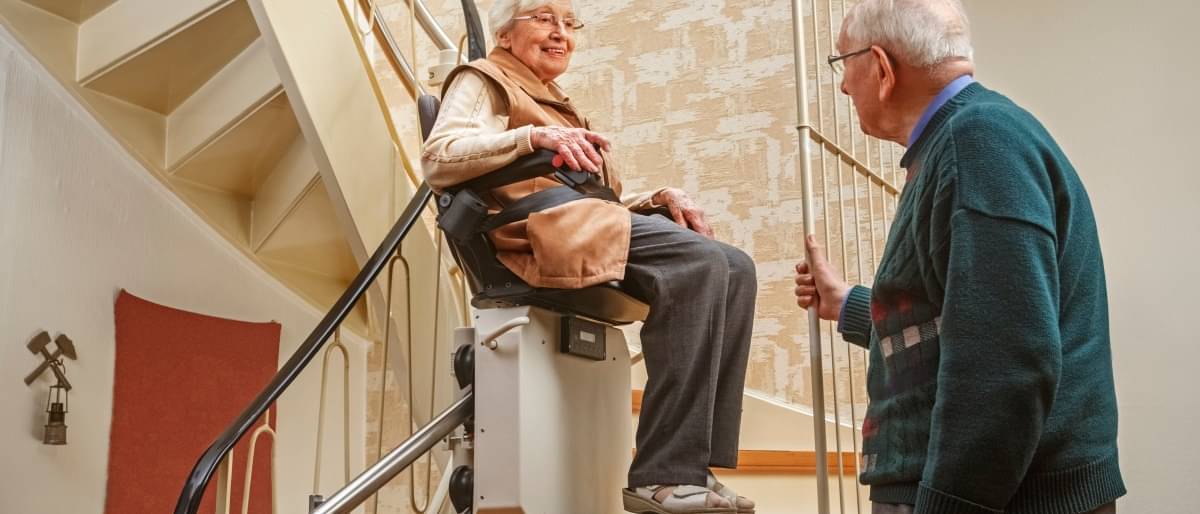 Älteres Paar fährt mit einem Treppenlift eine Treppe hinauf - Treppenlift Kosten