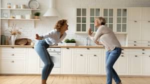 Eine Frau und ihre Mutter tanzen vor Freude ausgelassen durch ihre neue, helle Küche.