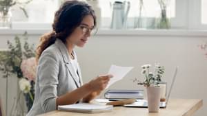 Junge Frau mit Blazer schaut auf eine Rechnung.