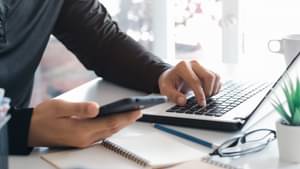 Geschäftsmann mit Smartphone inder Hand sitzt am Laptop