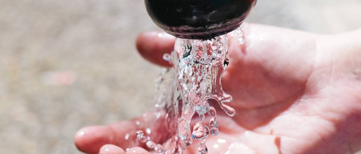 Wasser läuft aus dem Hahn in die Hand - Brunnen bohren kosten