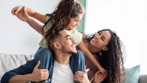 Junger Mann hat seine Tochter auf den Schultern, die Tochter Spielt mit der Mutter, alle lachen. 