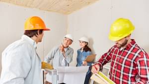 Vier Personen mit Schutzhelmen stehen in einem frisch renovierten Raum.