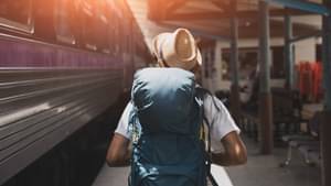 Ein Backpacker mit Hut und Rucksack läuft entspannt an einem Zug entlang.