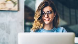 Frau mit Brille schaut lächelnd in ihren Computer