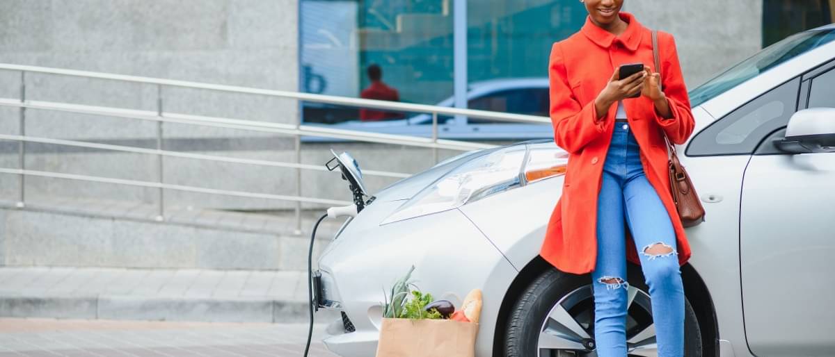Frau steht vor Elektroauto und Tankt Strom - E-Mobilität 