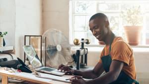Junger Mann mit Schürze sitzt an einem Schreibtisch.