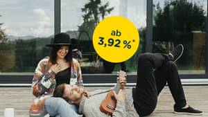 Pärchen sitzt auf einer Holzterrasse vor dessen Haus; Zinssatz ab 3,92 % p.a.*