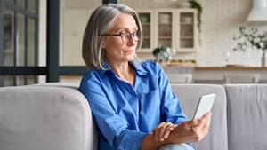 Ältere Frau in blauer Bluse schaut konzentriert auf ihr Smartphone.