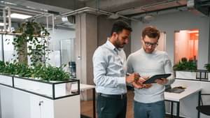 Zwei Kollegen stehen im Büro und schauen gemeinsam auf ein Tablet.