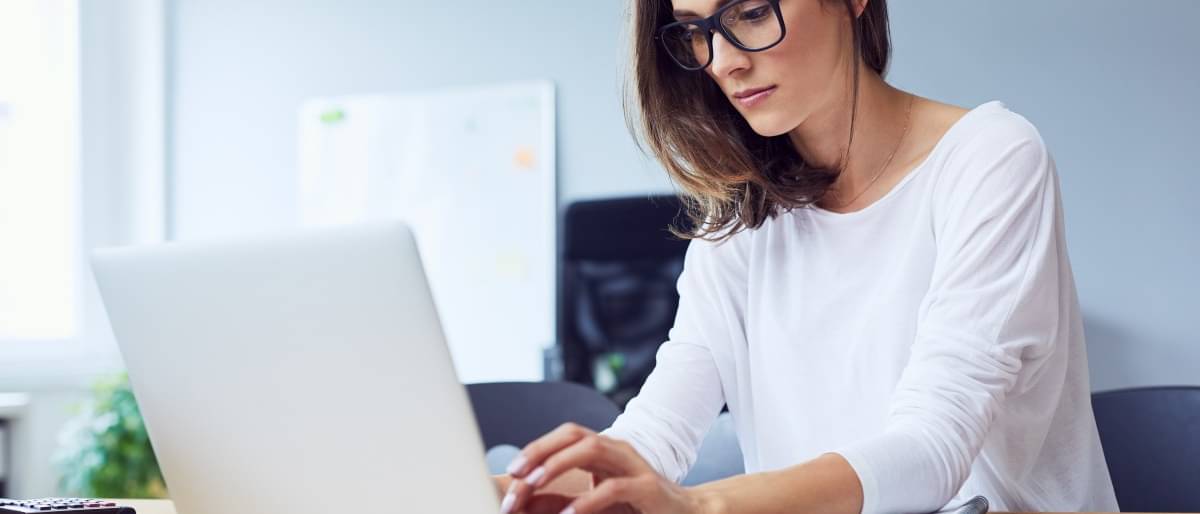Junge Frau mit Brille tipp konzentriert auf ihrem Laptop.