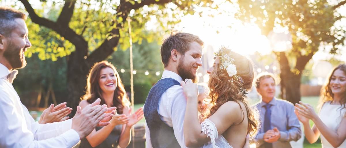 Tanzendes Brautpaar zwischen klatschenden Gästen bei Sonnenuntergang auf einer Wiese - Hochzeit planen