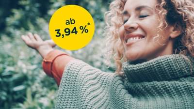Frau steht glücklich im Wald und breitet die Arme aus: Klimakredit ab 4,94% p.a.*