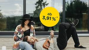 Pärchen sitzt auf einer Holzterrasse vor dessen Haus; Zinssatz ab 3,91 % p.a.*