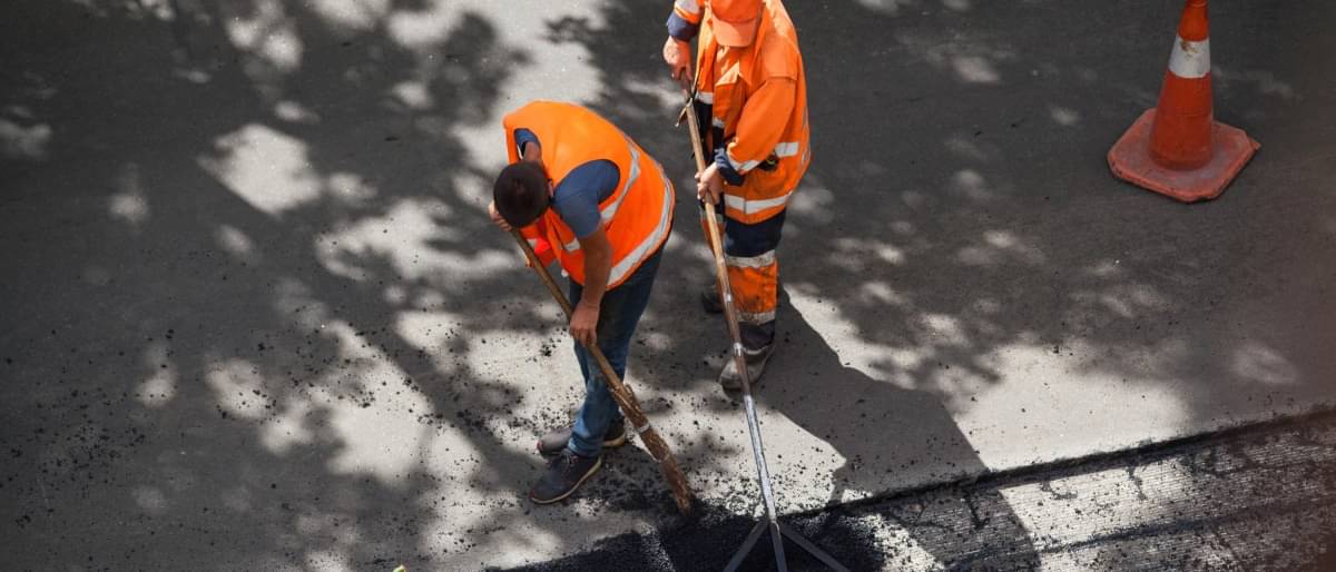 Straßenbauarbeiter in orangefarbener Schutzkleidung reparieren eine Straße