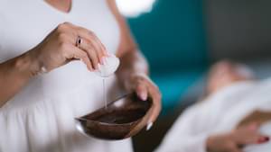 Eine Heilpraktikerin steht in einem Behandlungsraum und tunkt einen Wattebausch in eine Flüssigkeit, um die Behandlung eines Patienten vorzubereiten