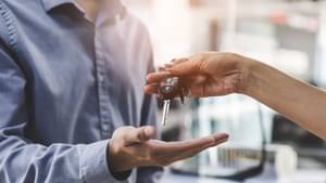 Verkäuferin übergibt den Schlüssel eines neuen Autos an den Käufer.