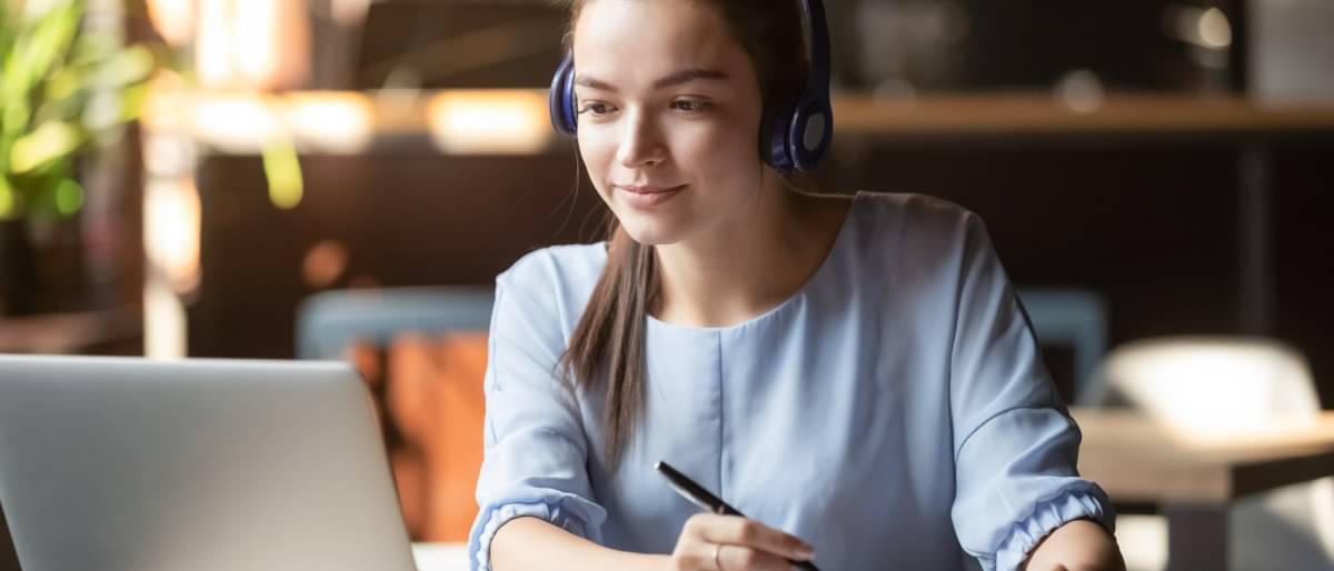 Eine junge Frau sitzt mit Kopfhörer vor ihrem Laptop - Fernstudium Kosten