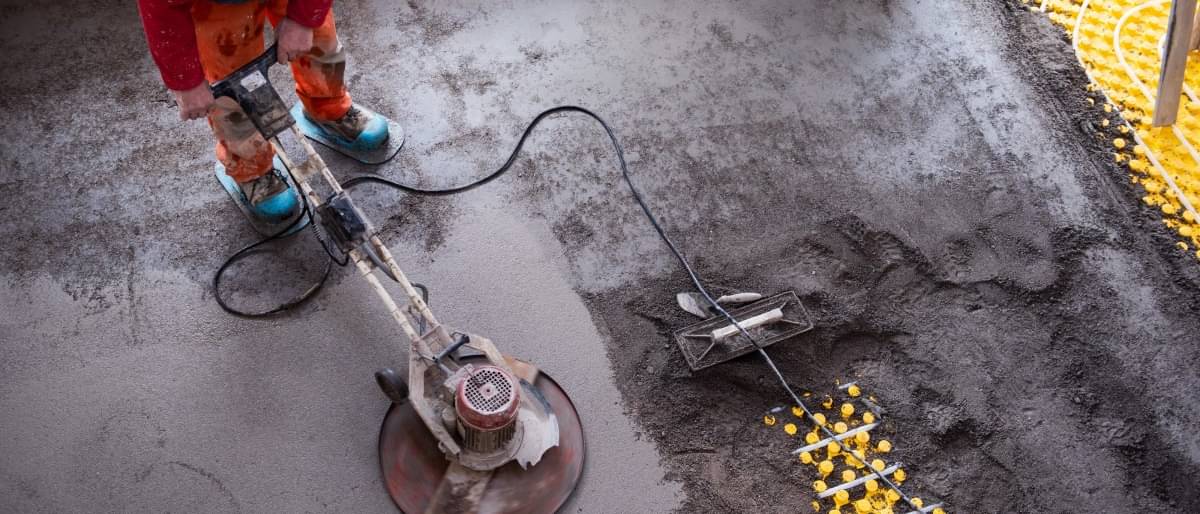 Ein Handwerker verteilt mit einer Maschine grauen Estrich auf dem Boden eines Neubaus.