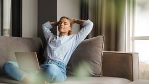 Frau sitzt mit Laptop entspannt auf dem Sofa und streckt sich. Tilgung von Kredit und Darlehen verstehen. 