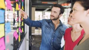 Drei Kollegen sprechen über Post-Its an einer Glaswand.