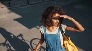 Eine junge Frau steht lässig neben ihrem Fahrrad und schirmt mit der Hand ihr Gesicht vor der Sonne.