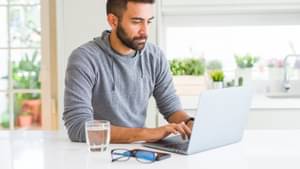 Ein junger Mann sitzt konzentriert am Laptop.