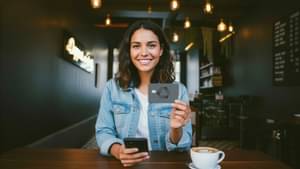 Eine junge Frau sitzt im Café und zeigt ihre neue Commerzbank Girocard