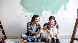 Familie sitzt auf dem Boden vor einer Wand, die angefangen wurde in Türkis zu streichen.