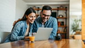 Eine Frau und ein Mann sitzen fröhlich an einem Laptop und informieren sich über thesaurierende Fonds.
