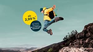 Ein Mann mit gelber Jacke und Rucksack springt von einem Felsabsatz mit abgespreizten Armen herunter. Ratenkredit ab 2,99% p.a.* und zusätzlichen Zinsvorteil bei Online-Abschluss von bis zu 0,6% p.a.**