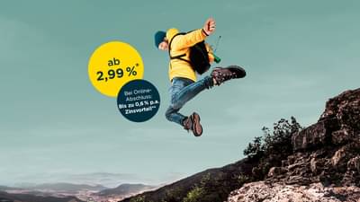 Ein Mann mit gelber Jacke und Rucksack springt von einem Felsabsatz mit abgespreizten Armen herunter. Ratenkredit ab 2,99% p.a.* und zusätzlichen Zinsvorteil bei Online-Abschluss von bis zu 0,6% p.a.**