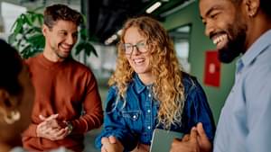 Zwei Frauen und zwei Männer stehen zusammen fröhlich lachend in einem Büro. Die zwei Frauen geben sich die Hände.