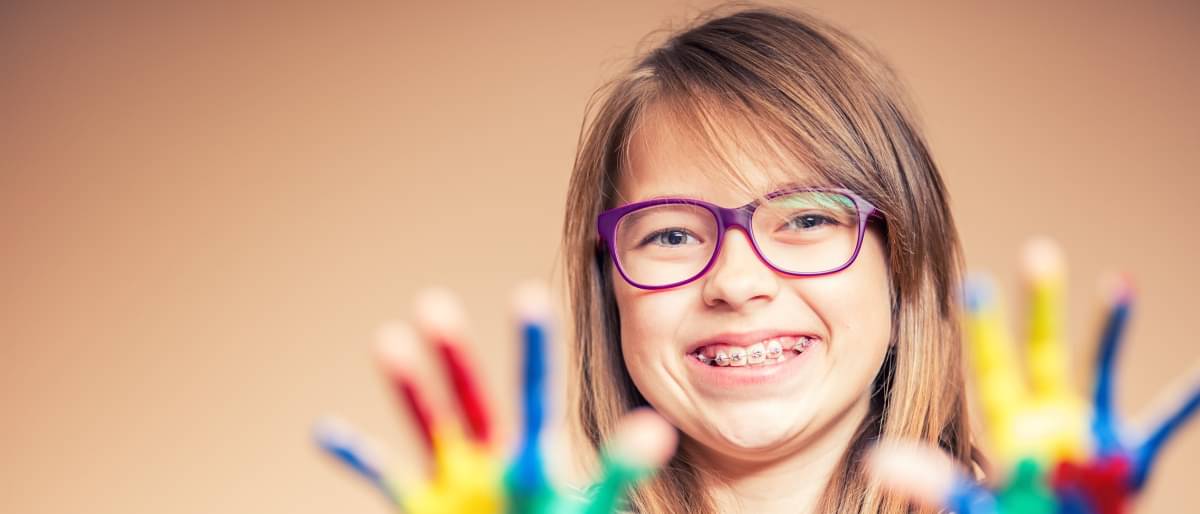 Mädchen mit Brille zeigt ihre bunt bemalten Hände - Zahnspange Kosten